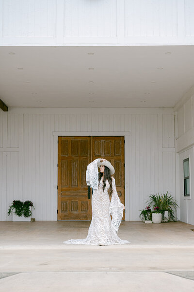 Boho bride in a lace gown poses in front of the wooden doors at The Videre Estate wedding venue in Austin, Texas.
