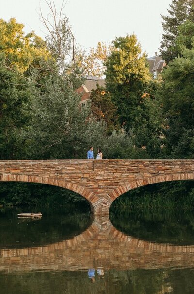 Couple standing on a bridge in Boulder with their reflection in the water during romantic engagement photos