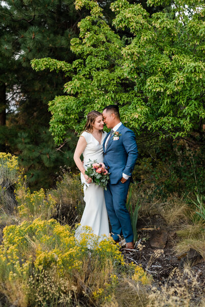 A groom in a blue suit nuzzles into his bride.