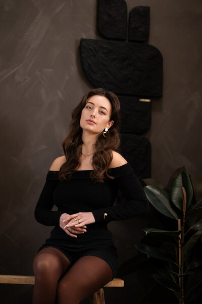 Stijlvolle brandingshoot in Studio Laurant, met een houten bankje tegen een zwarte muur en een handgemaakt kunstwerk als artistieke achtergrond.