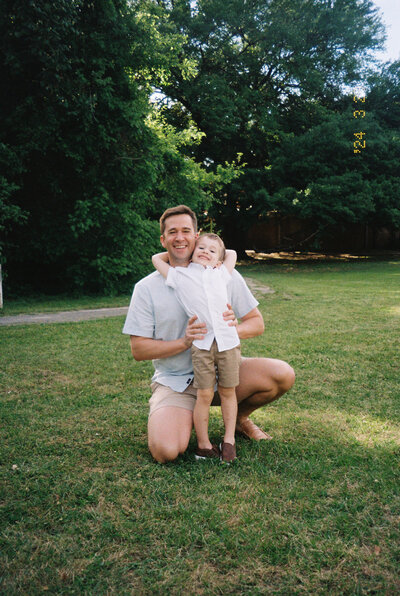 portrait of a father and son with son standing in front of kneeling dad