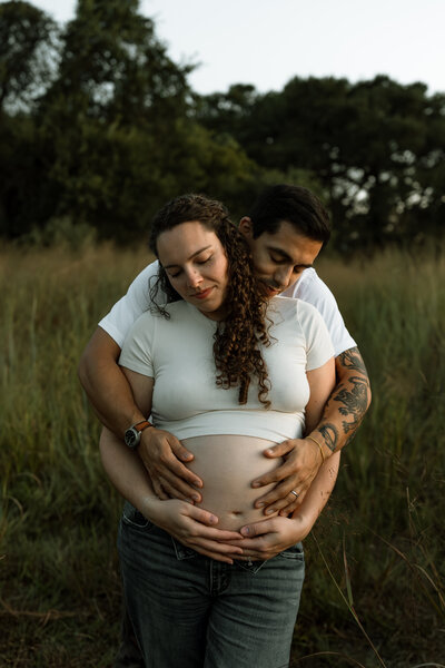 Pregnant woman and husband hugging her while standing in field