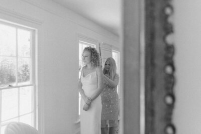 Mother of the bride zipping up her daughter’s wedding dress, captured through a mirror reflection during a quiet getting-ready moment before an intimate backyard ceremony in Richmond, Virginia.