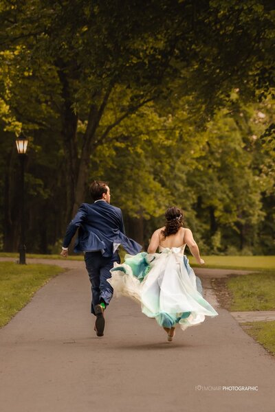 Bride and groom running down park path