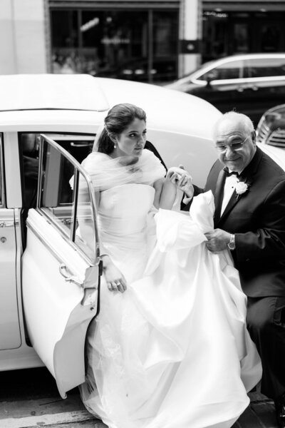 father of the bride helping bride get out of classic car