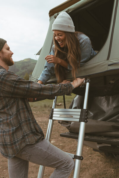 Husband stands laughing with his wife whio is laying in their camper at