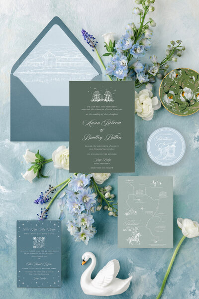 Wedding invitation suite with a Montana flair, featuring white foil stamping on blue and green paper, a custom round tag, and an illustrated map—showcasing creative wedding invitation ideas.