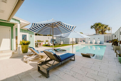 pool with loungers in pool and on deck, grassy lounge area with couch and chair set