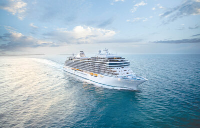 Luxury ocean cruise ship sailing across open blue waters under a bright sky.