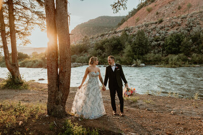 Bride and groom walk hand-in-hand through a scenic field with the Maroon Bells mountains as the backdrop at their summer wedding.