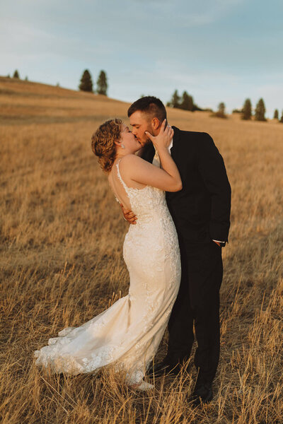 Bride and groom kissing at sunset in open field
