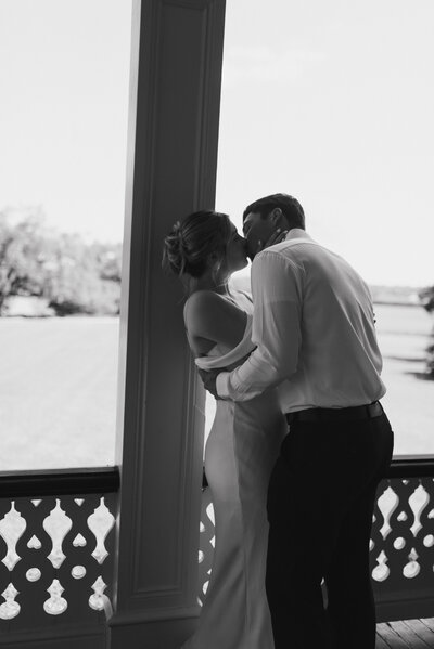 a black and white photo of a wedding couple kissing on the Jefferson House porch at Rip Van Winkle Gardens in Louisiana. 