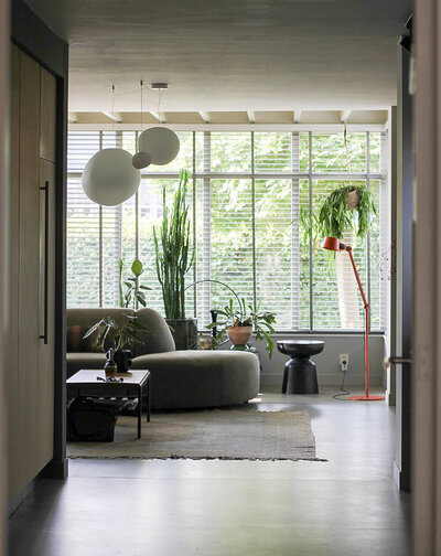 Ruime, lichte woonkamer met grote ramen, natuurlijke tinten en minimalistisch meubilair, ontworpen door LOOSZ.
