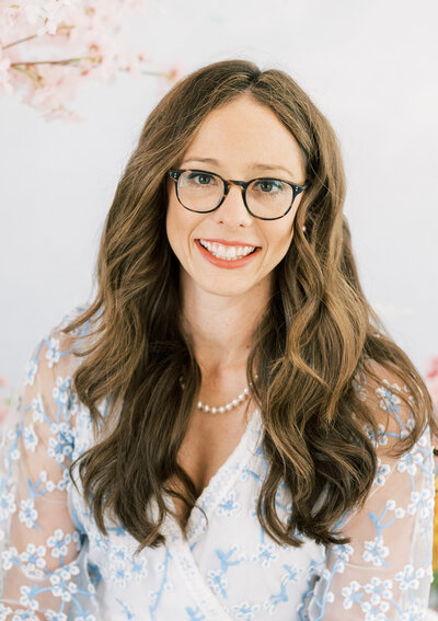 Headshot of photographer with glasses and curly brown hair smiling and wearing pearls