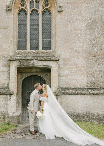 chloe-winstanley-weddings-cotswolds-bride-groom-church-door-kiss