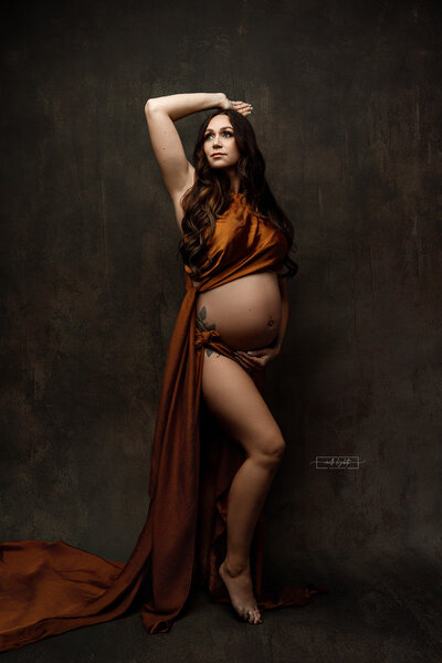 pregnant woman embracing her baby bump draped in fabric in studio session in East Jordan