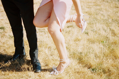 Photo of couples legs. Person in pink dress and white heels with bows