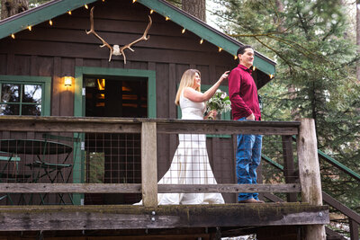Bride touching grooms shoulder for first look on porch of rustic cabin in the woods.