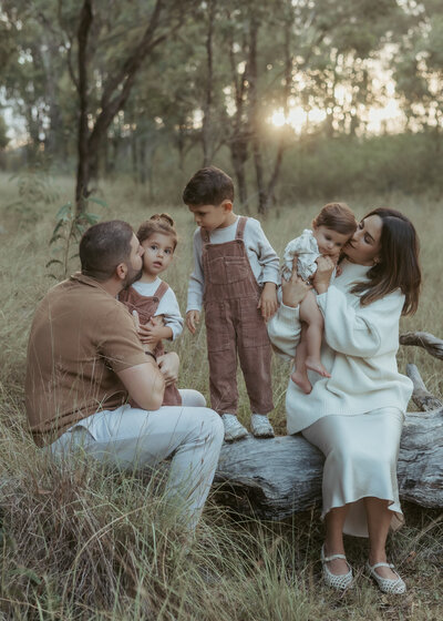 Beautiful family of five kissing and cuddling together on a log in a beautiful natural location for the family photography experience.