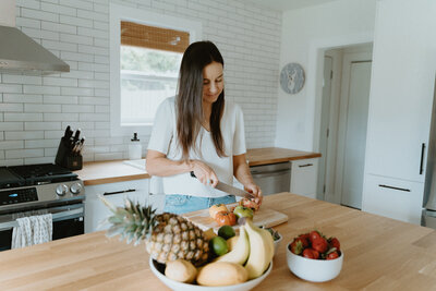 Woman cutting vegetables on a cutting board in a kitchen.