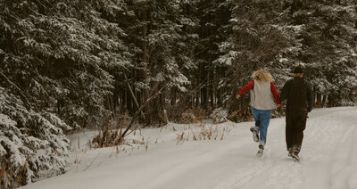 Man and woman running away from the camera in the snow in Idaho Falls, ID.