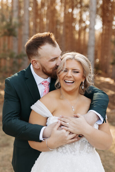 Groom kissing side of bride's temple while bride is laughing