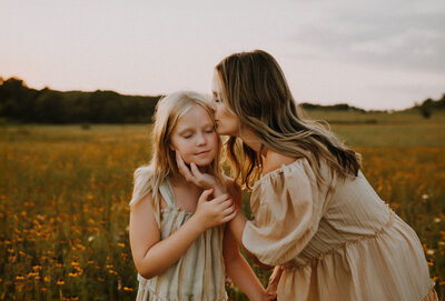 a mother kissing her daughters temple while standing in a field of yellow flowers in fort worth, tx