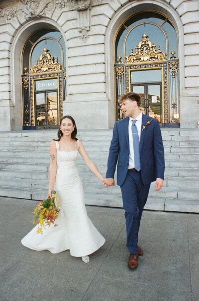 newlyweds walk in front of city hall building