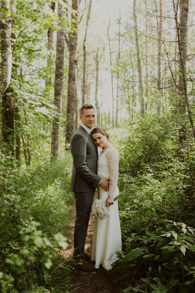 Wedding portrait of a couple standing in lush forest summer in Finland