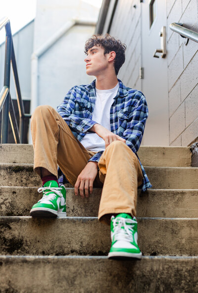 boy sitting on stairs with green nikes on and posing for senior photos