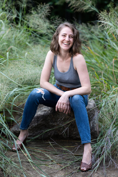 Raleigh Wedding Photographer smiles at camera as wind blows her har in her face as she huddles her sweaters towards herself and smiling