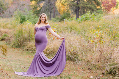 A beautiful pregnant woman wearing a purple dress in a green field.
