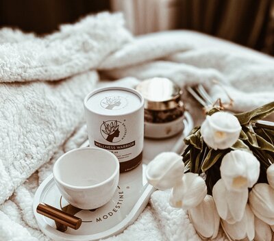 A woman's hand gently rests on a white teapot, capturing the moment before ceremony begins.