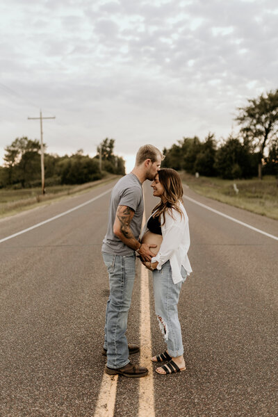 woman and man maternity shoot kissing in the road