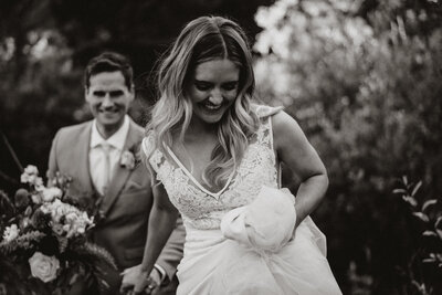 Bride and groom walking hand in hand, smiling joyfully in a forest after their Breckenridge wedding ceremony.