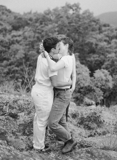 Cinematic wide shot of the couple embracing on the summit, with soft focus and natural light.
