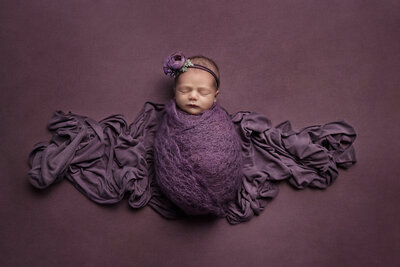 newborn baby girl wrapped in purple mohair crochet wrap with a purple flower headband.