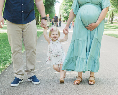 toddler walking next to parents during maternity photo session