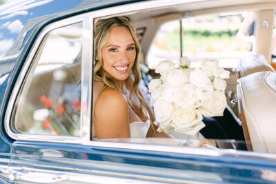 Bride smiling through the open window of a car at the VIP Gold Floor entrance of the Fairmont Banff Springs Hotel holding her bouquet and looking toward the camera after her wedding ceremony