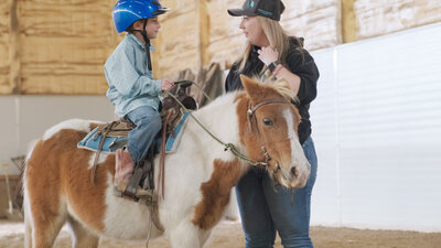 EAL Canada-certified facilitator guiding a child riding a horse in Spirit's Respite Ranch, a sanctuary offering inclusive kids' camps and riding lessons for kids in Central Alberta