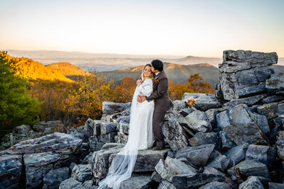  Bride and groom embracing on rocky mountaintop in Shenandoah with fall colors at
sunset
