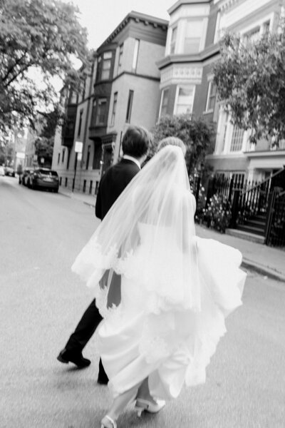 Chic bride and groom walk across a Chicago street after dark with skyline behind them