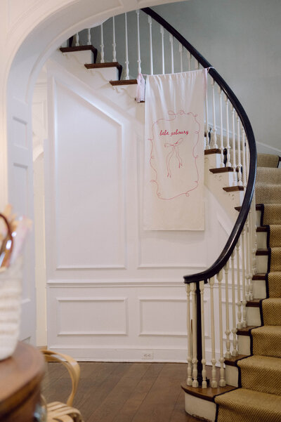 Curved staircase with a pink hand-stitched baby shower banner in a classic DC home, soft film look