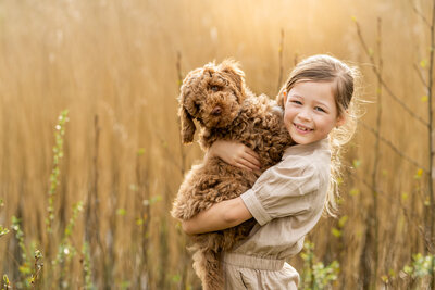 Lachend meisje dat haar labradoodle vasthoudt tijdens een outdoor fotoshoot in Herperduin, vastgelegd door Juliette Fotografie.