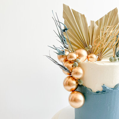 Close up image of blue and white birthday cake with gold decorations and a gold happy birthday sign.