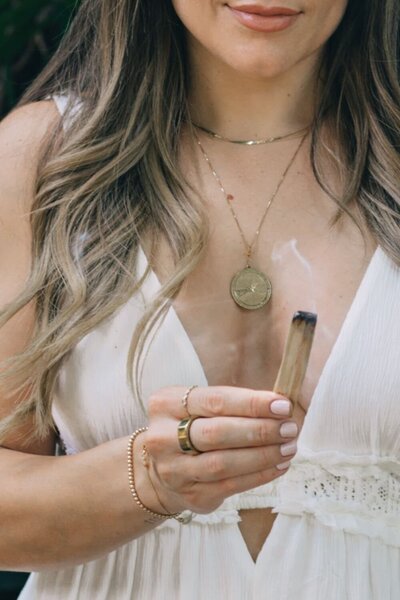 Close-up of Natalie Bernacchi holding a smoking palo santo stick during an energy clearing ritual for Reiki or healing work