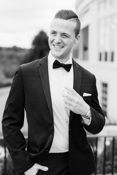 The groom wears a black tuxedo and smiles just before his wedding ceremony