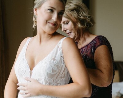 A bride smiles as her mother zips up her lace wedding gown for her Boulder wedding day at the St Julien Hotel. Photo by Haley Hawn.