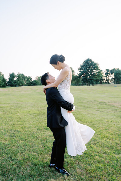 Groom lifting up bride in a grassy field photo taken by Austin wedding photographer