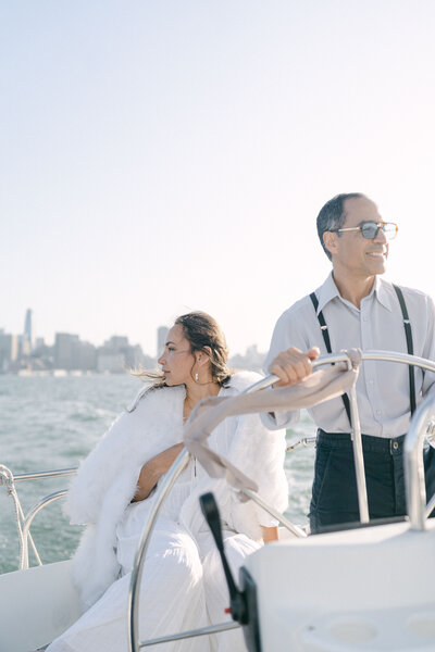 Couple on sailboat looking off with the San Francisco skyline in the background